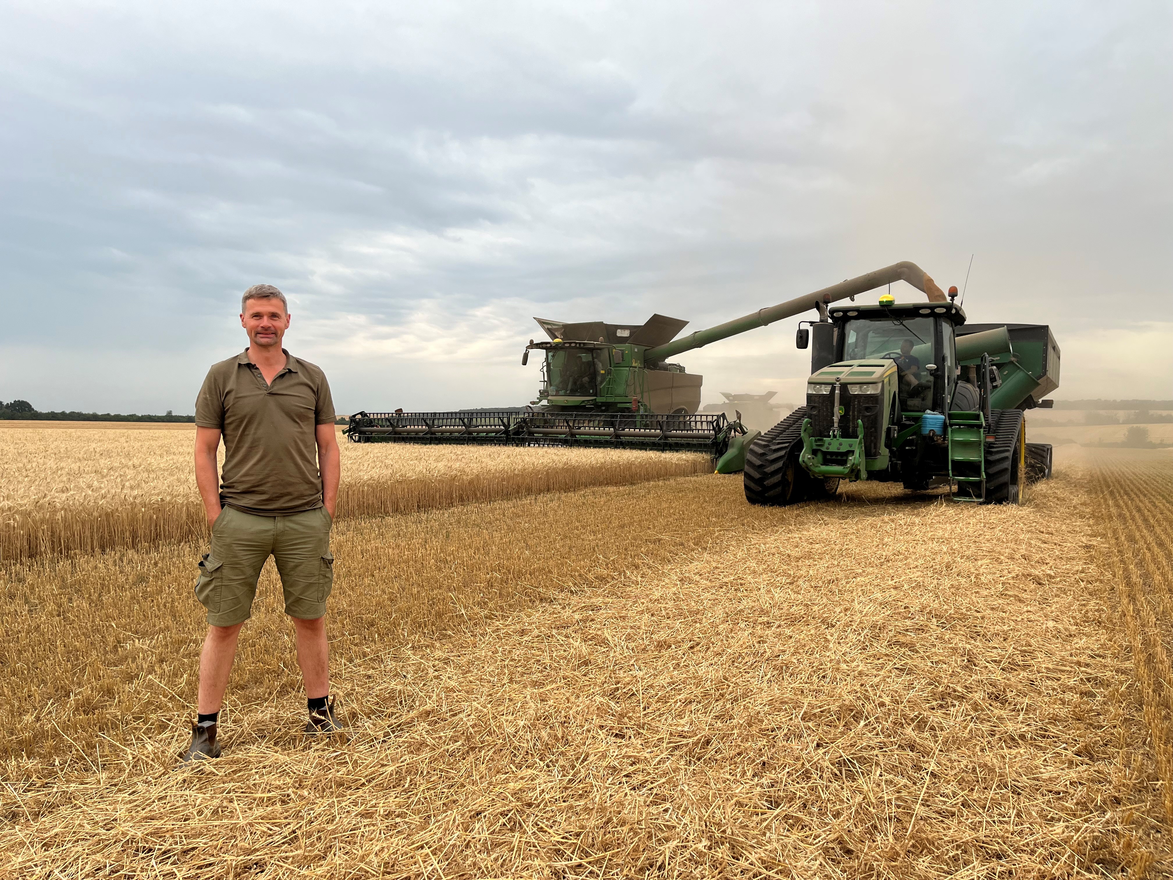 Kees on a wheat field in Ukraine. A big machine is harvesting the wheat.