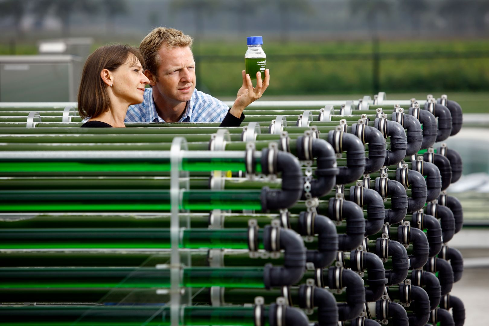 Twee onderzoekers bekijken een fles die een vloeistof met algen bevat