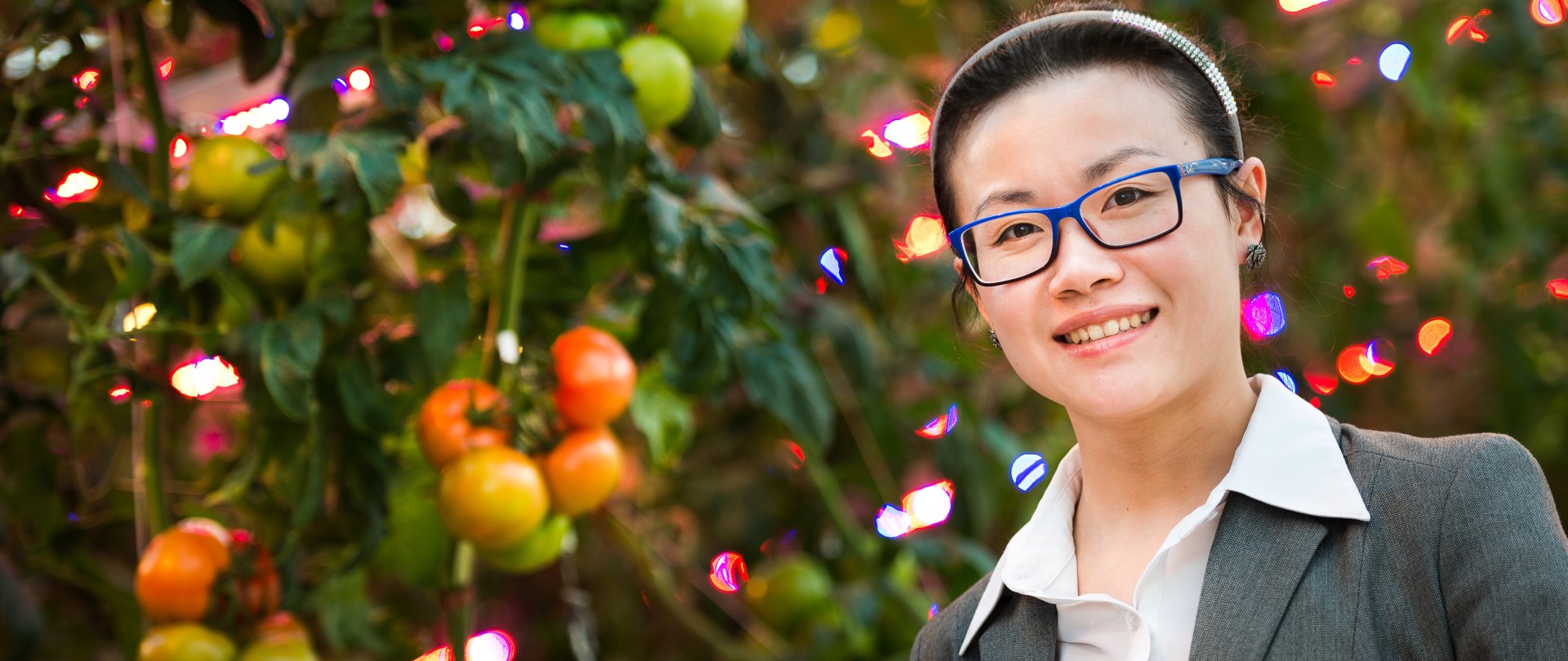 Portretfoto van Didi Qian. Ze staat voor tomaten met enkele kerstlichtjes.