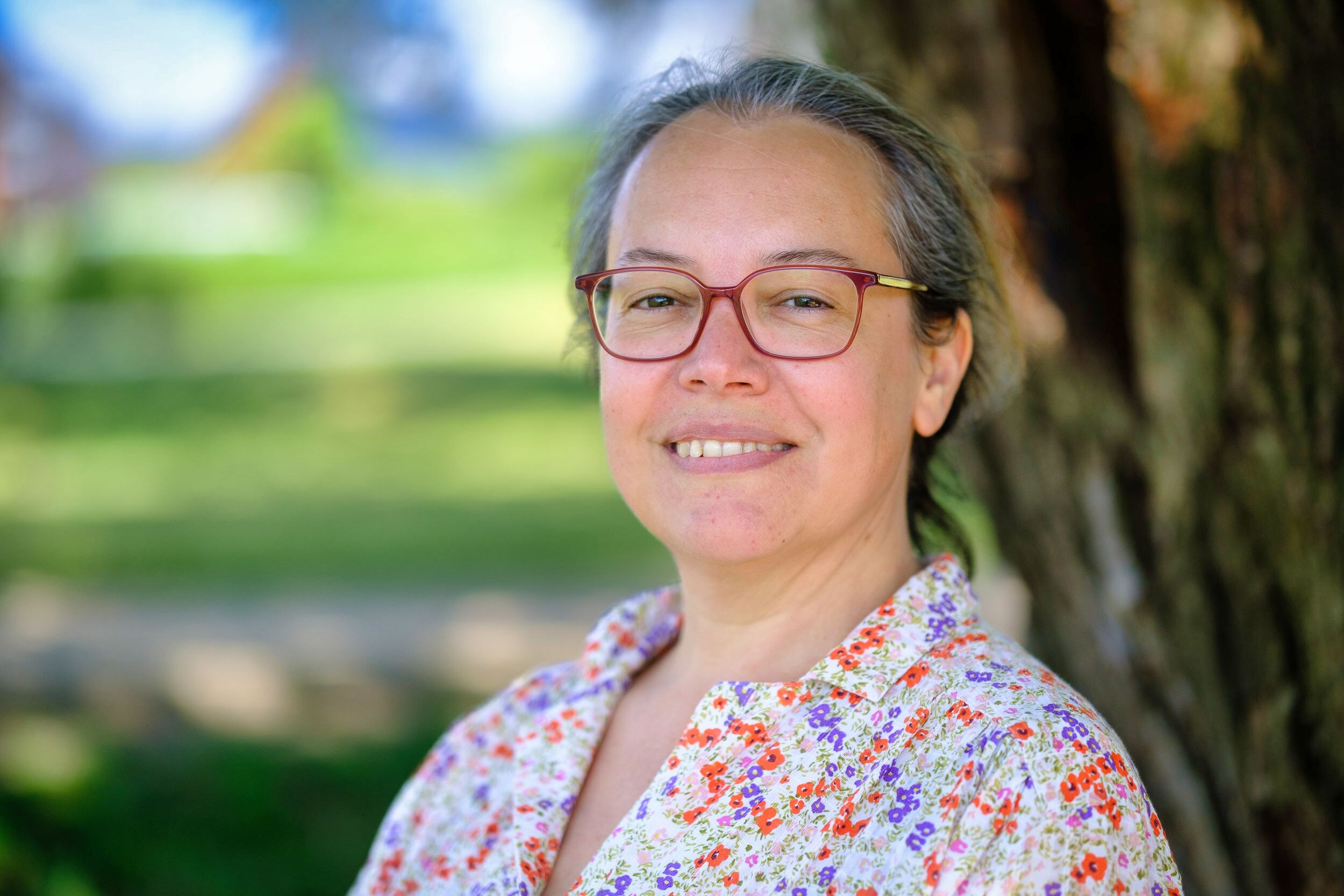 Marcia Bodero portrait photo, she is smiling to the camera. She is wearing red glasses.