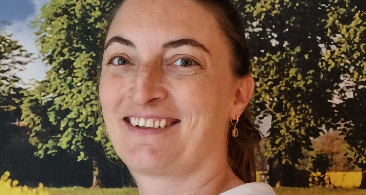 potrait picture of woman smiling towards the camera. In the background, there's a picture of trees in a field.