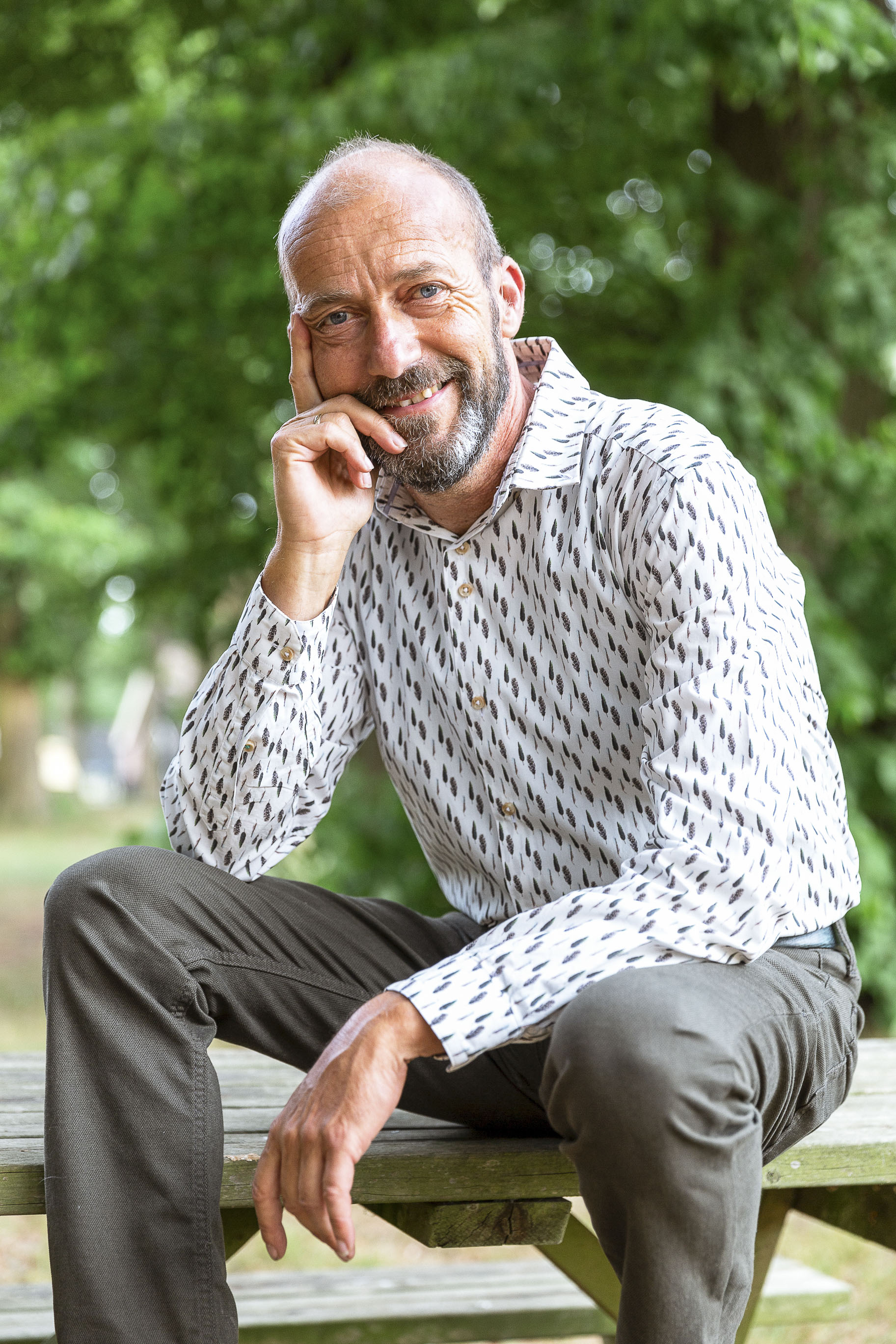 Reinier van den Berg posing in front of a camera. He is sitting on a picknick table.
