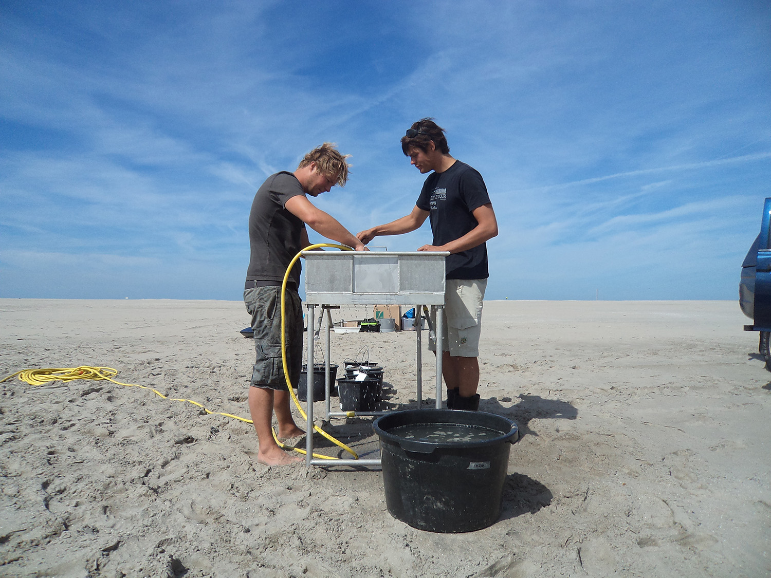 Two researchers taking benthos samples on an expansive beach