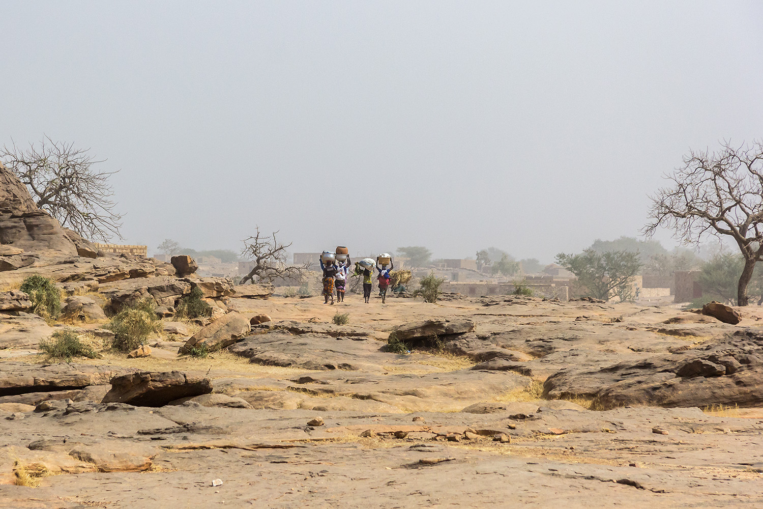 People carrying water in pots on their heads through a rocky desert