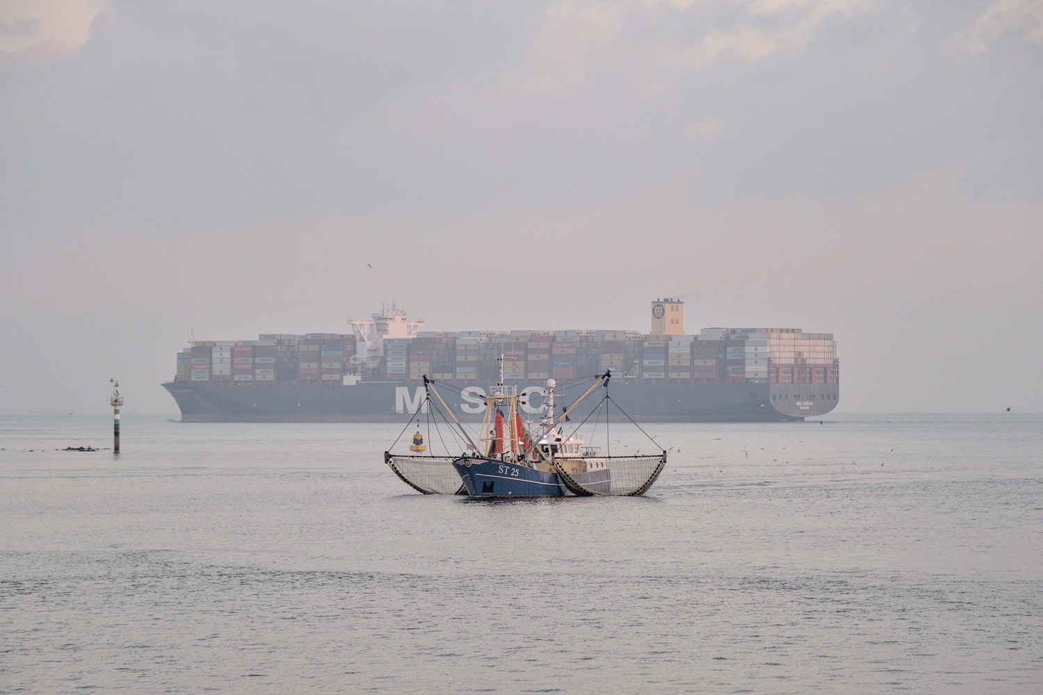 A fishing boat with a large cargo ship on the background