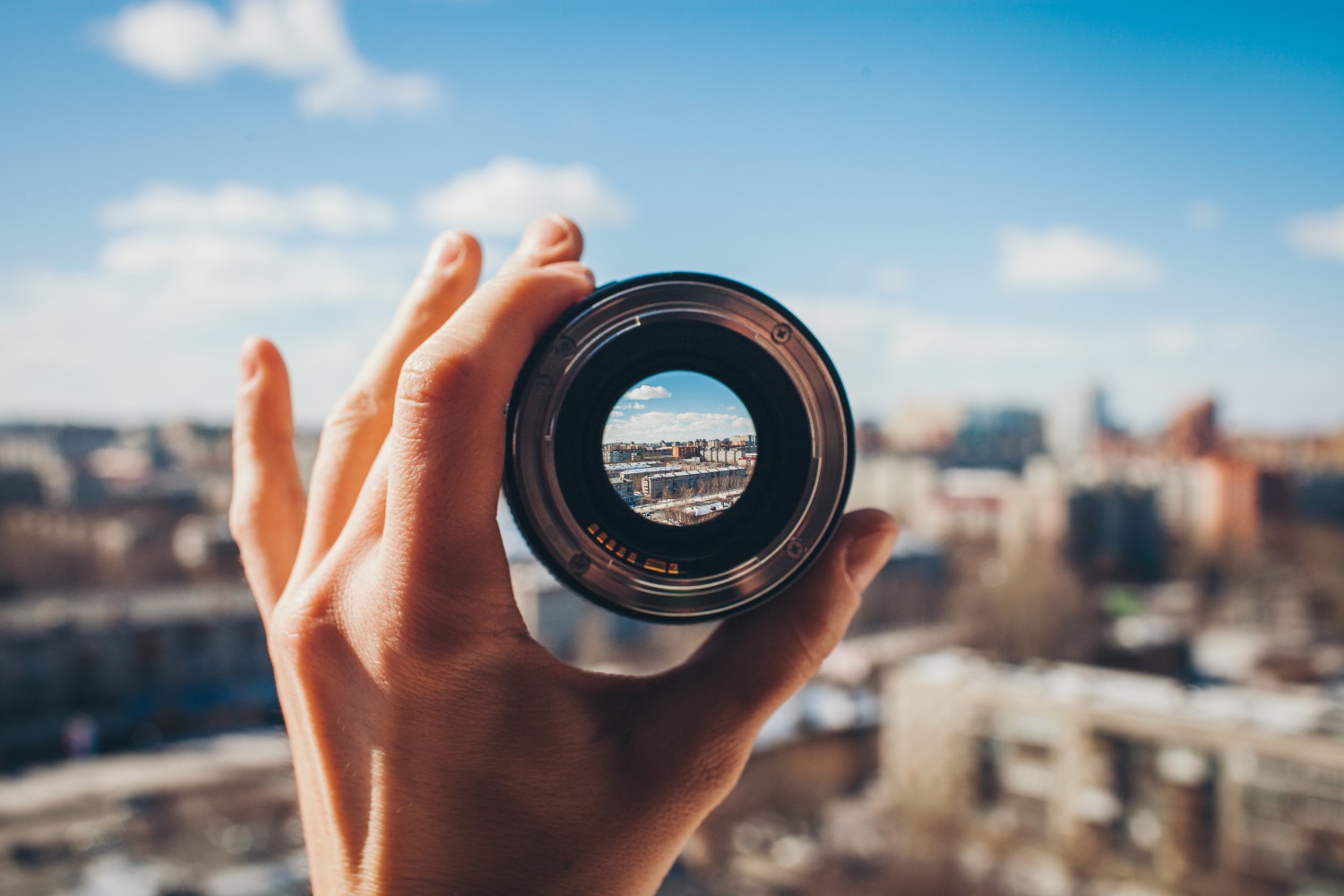 Een hand die een cameralens vasthoudt waardoor een stad te zien is