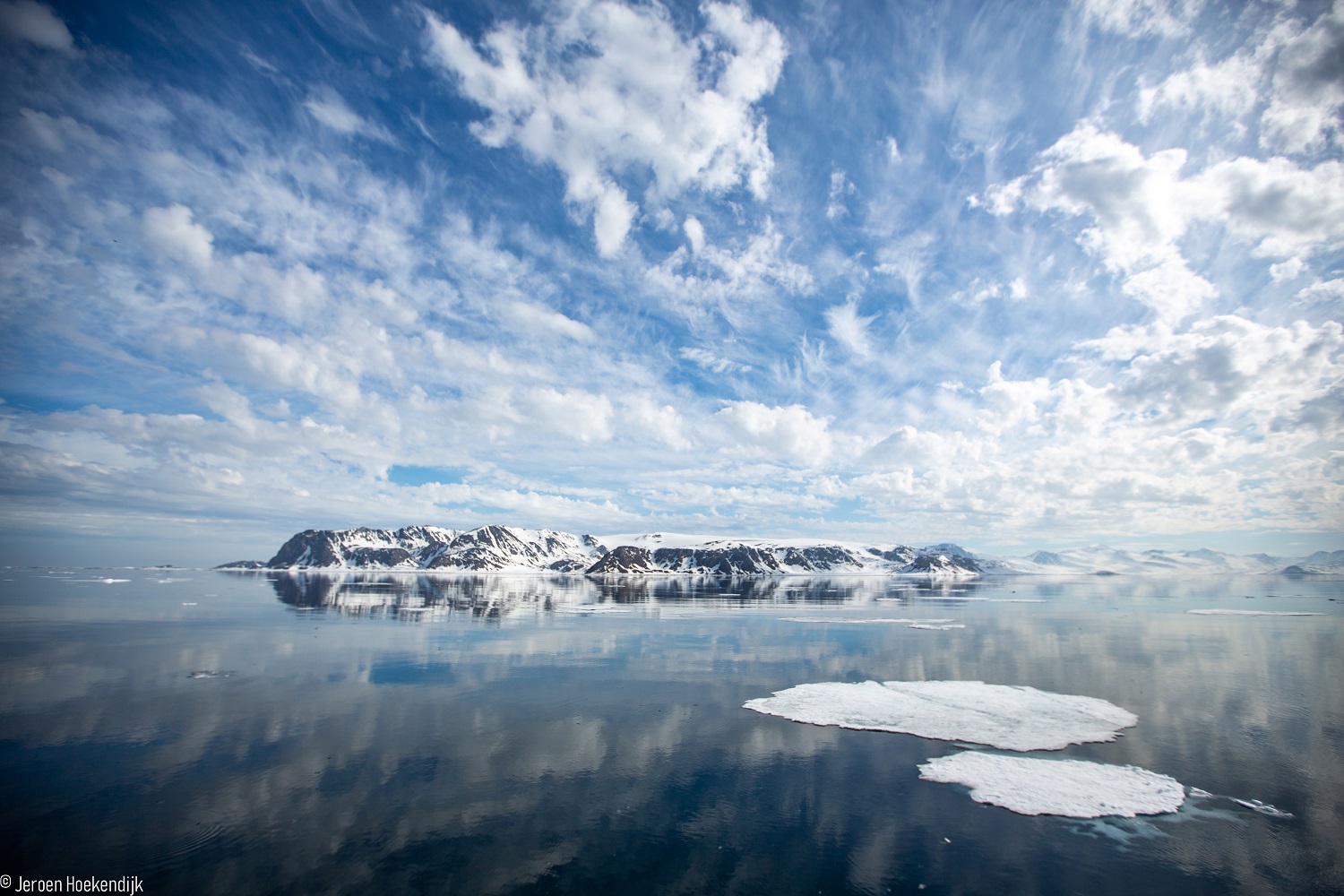 A photo of the ocean in the north pole with snowy mountains in the background