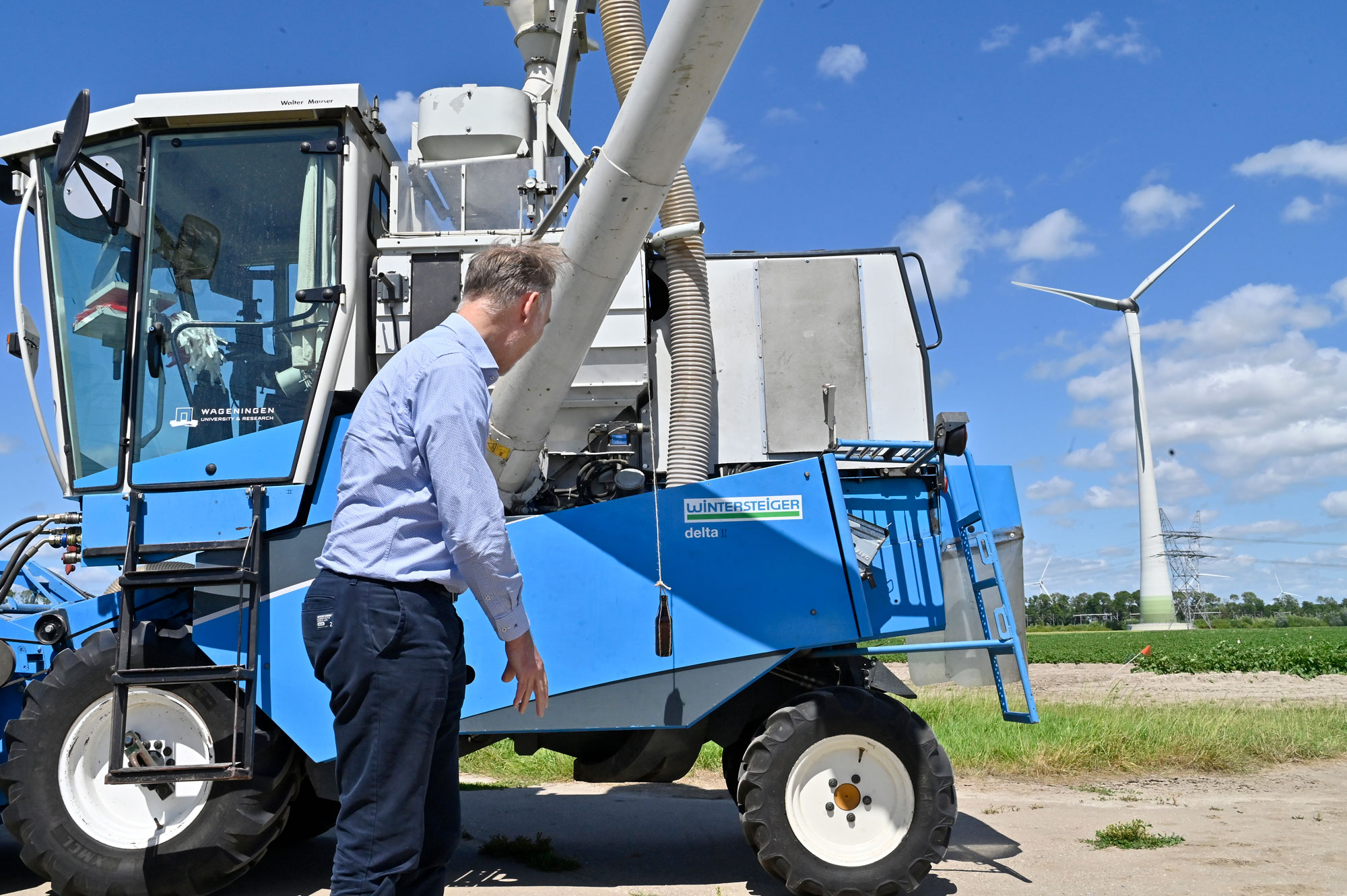 Man staat naast een blauwe tractor in het veld