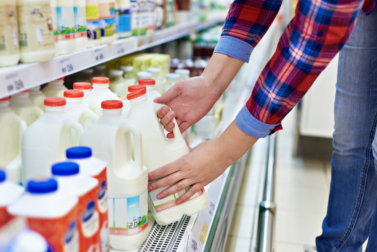 Twee handen pakken een rood pak melk op in de supermarkt.