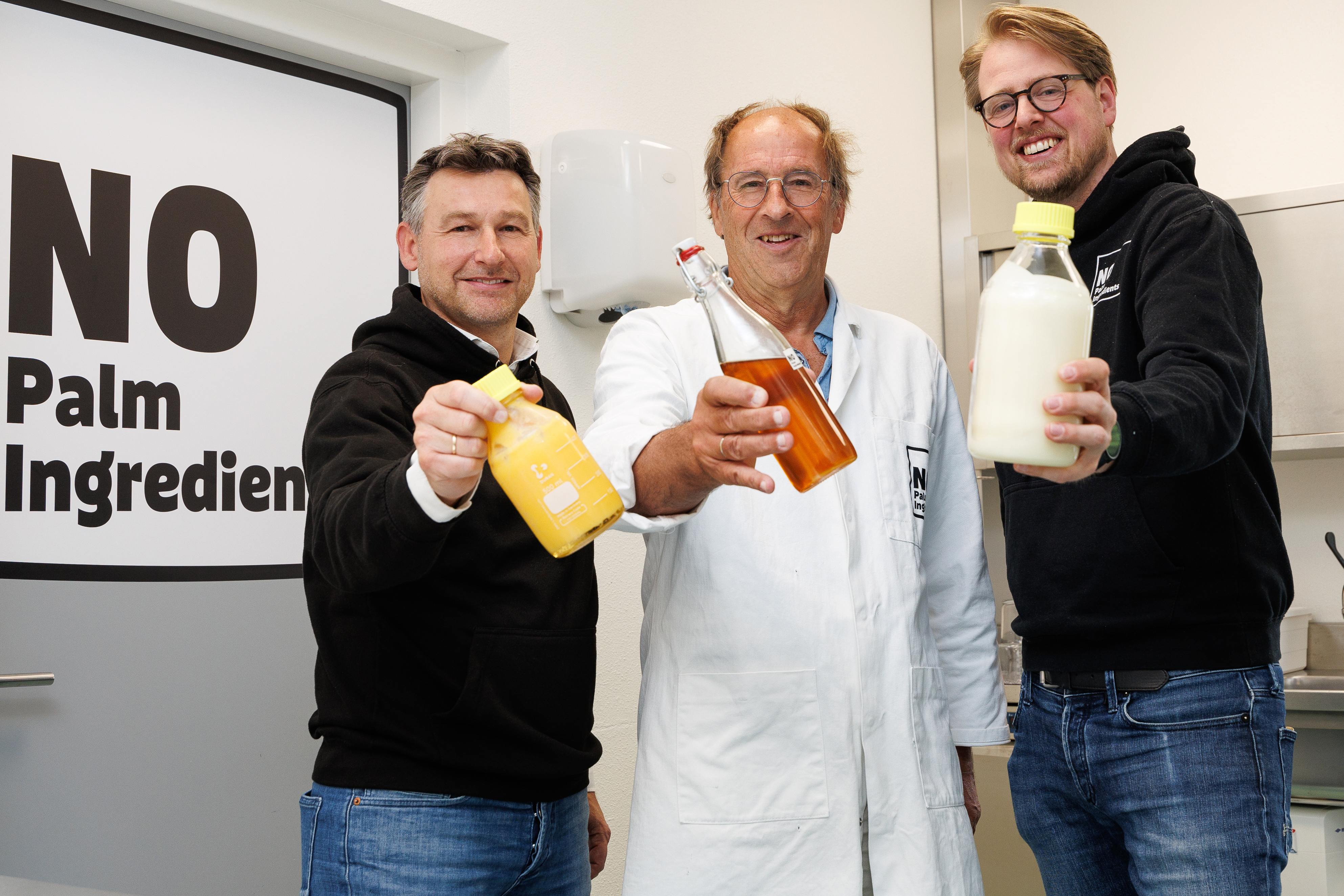 Three men from NoPalm Ingredients each show a bottle with NoPalm products