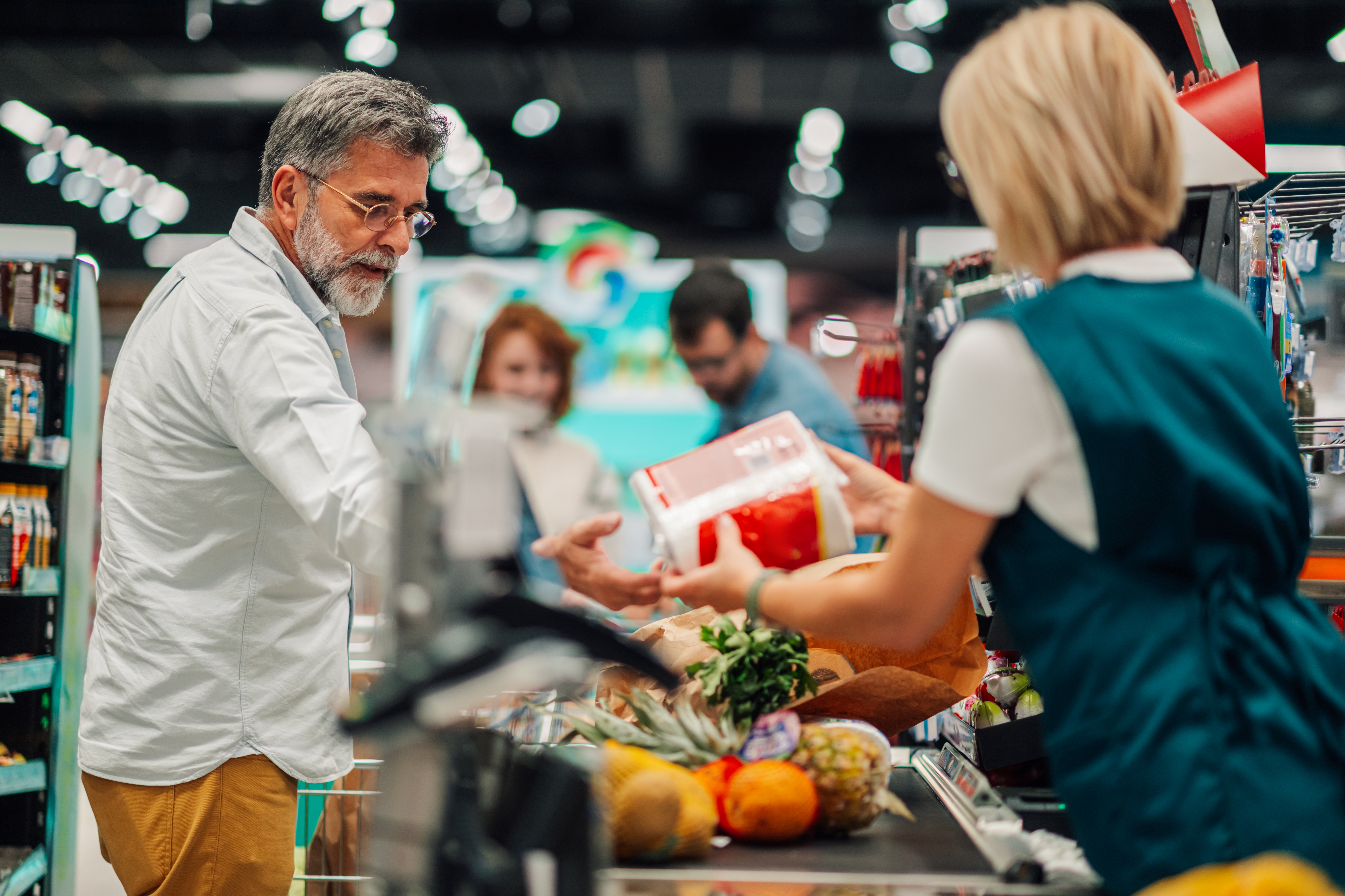Kassamedewerker scant boodschappen van senior klanten bij de kassa in de supermarkt
