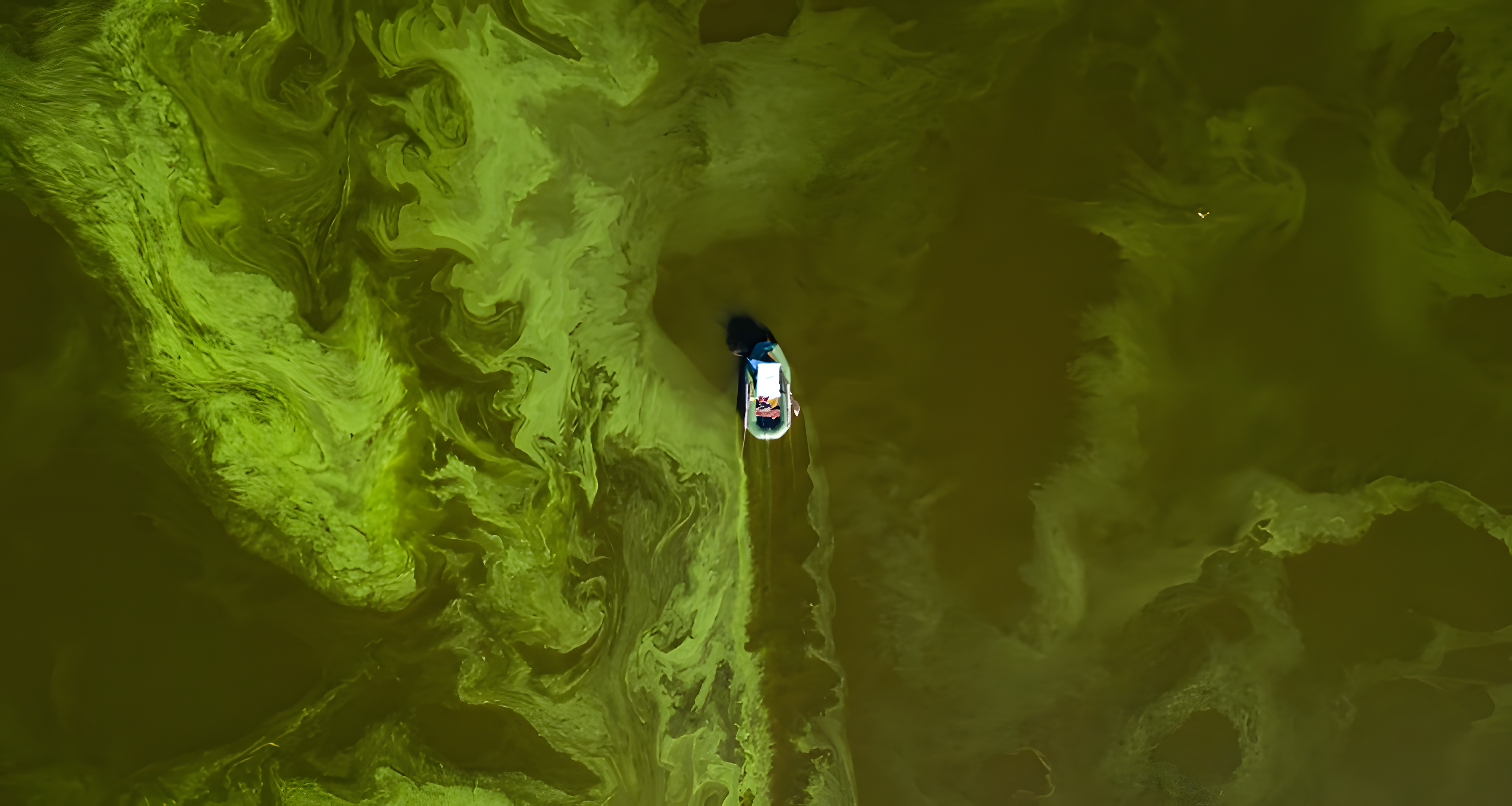 Boat sailing through a river that is green due to pollution, seen from a bird's-eye view