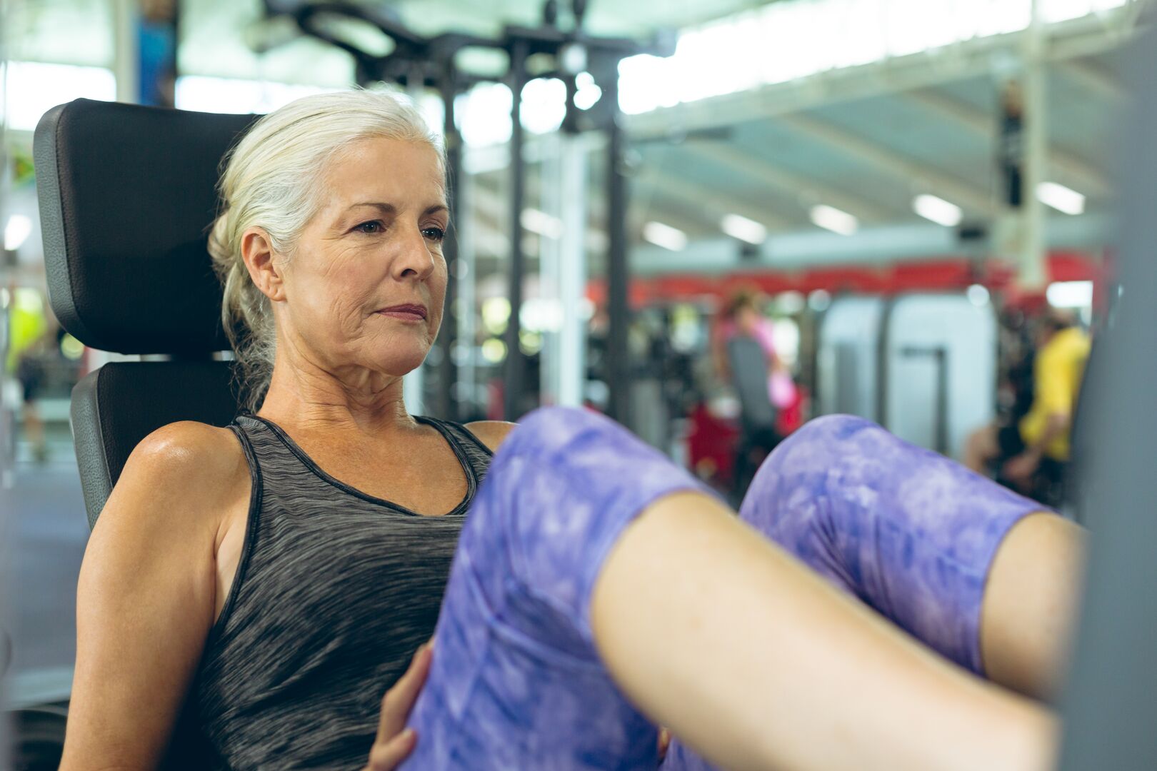 Een oudere vrouw is aan het trainen op een leg press fitnessapparaat
