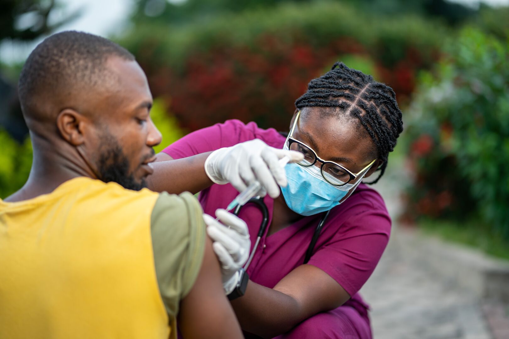Een man ontvangt een vaccinatie in zijn schouder van een verpleegkundige met een mondkapje op