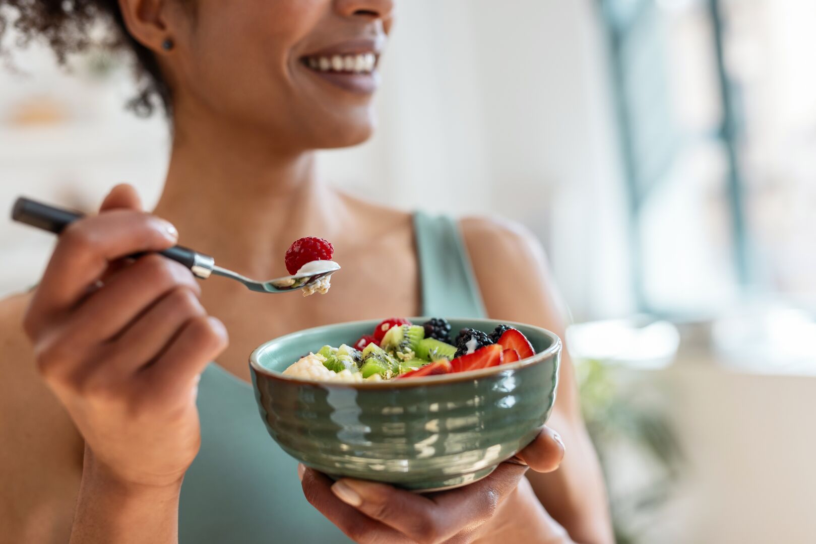 Een foto van een vrouw die met een lepel een hap neemt uit een ontbijtschaaltje met havermout en fruit