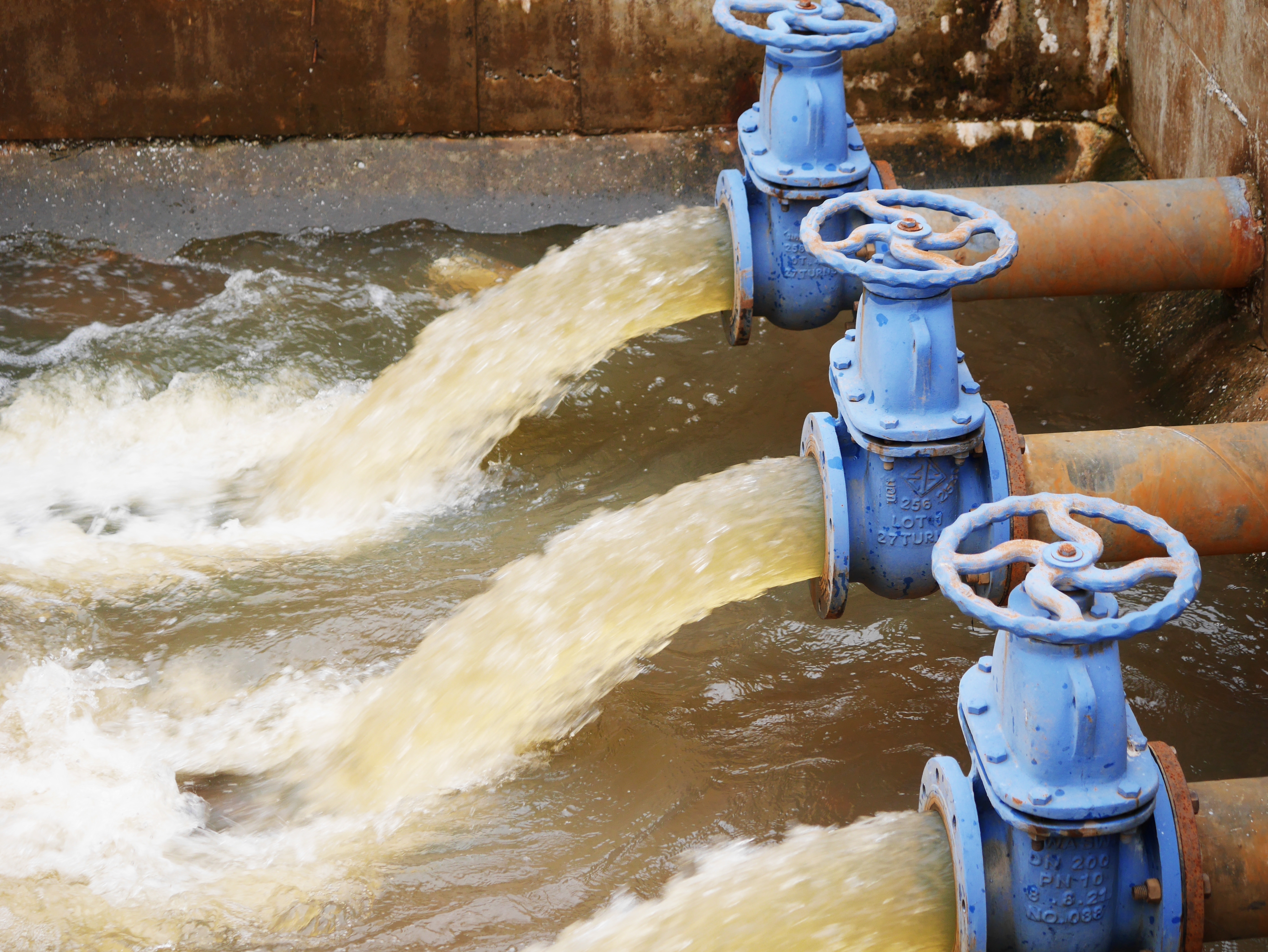Industrieel afwateringssysteem met vijf blauwe leidingen die water in een reservoir lozen. 
