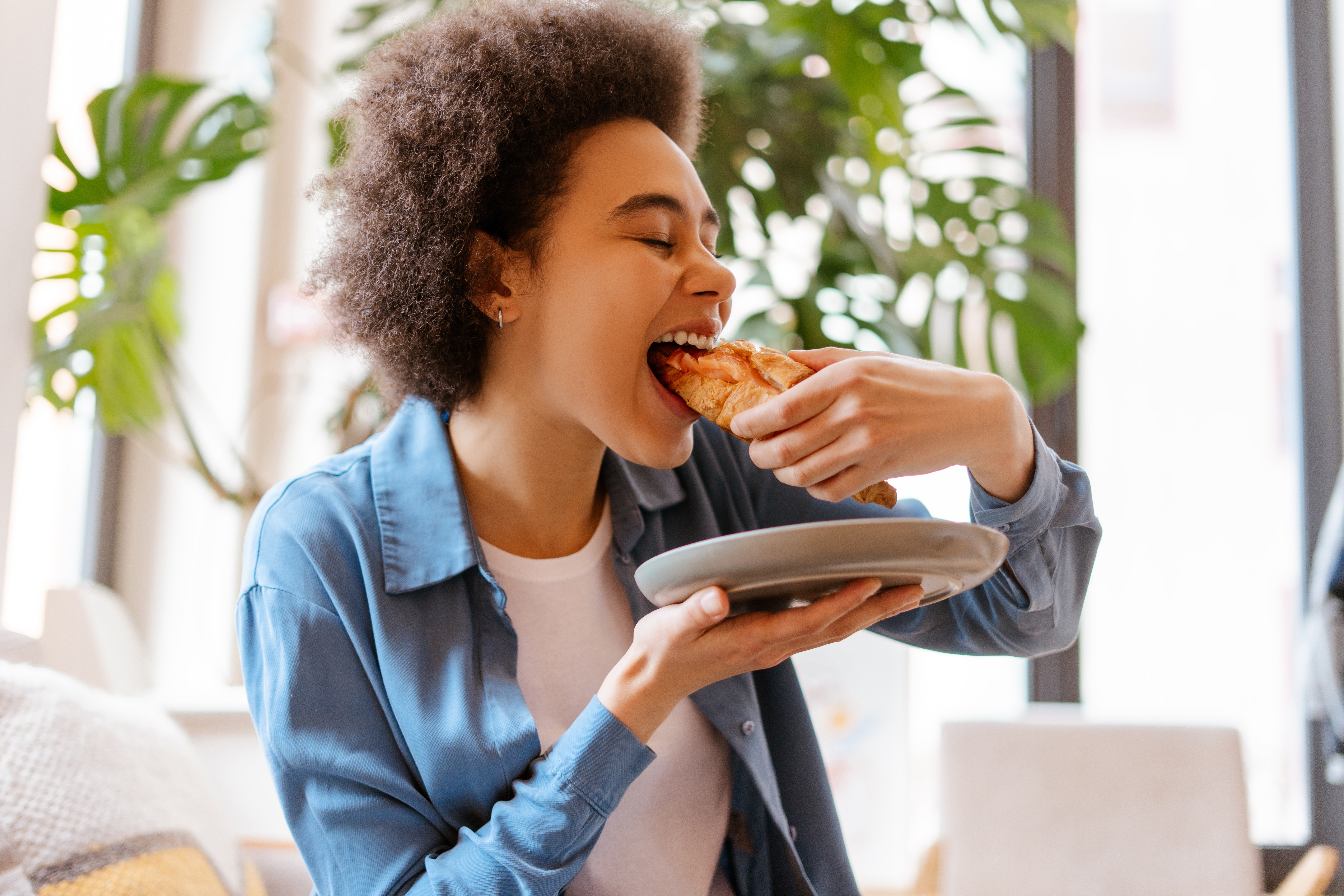 Een jonge vrouw eet een verse croissant terwijl ze op een comfortabele bank zit.