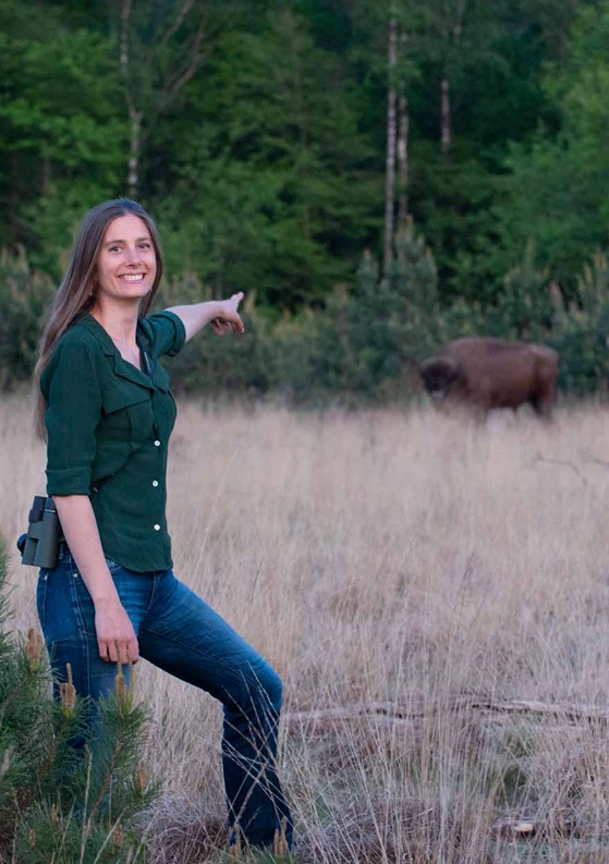 Vrouw in grasveld wijst naar bison bij bosgrens