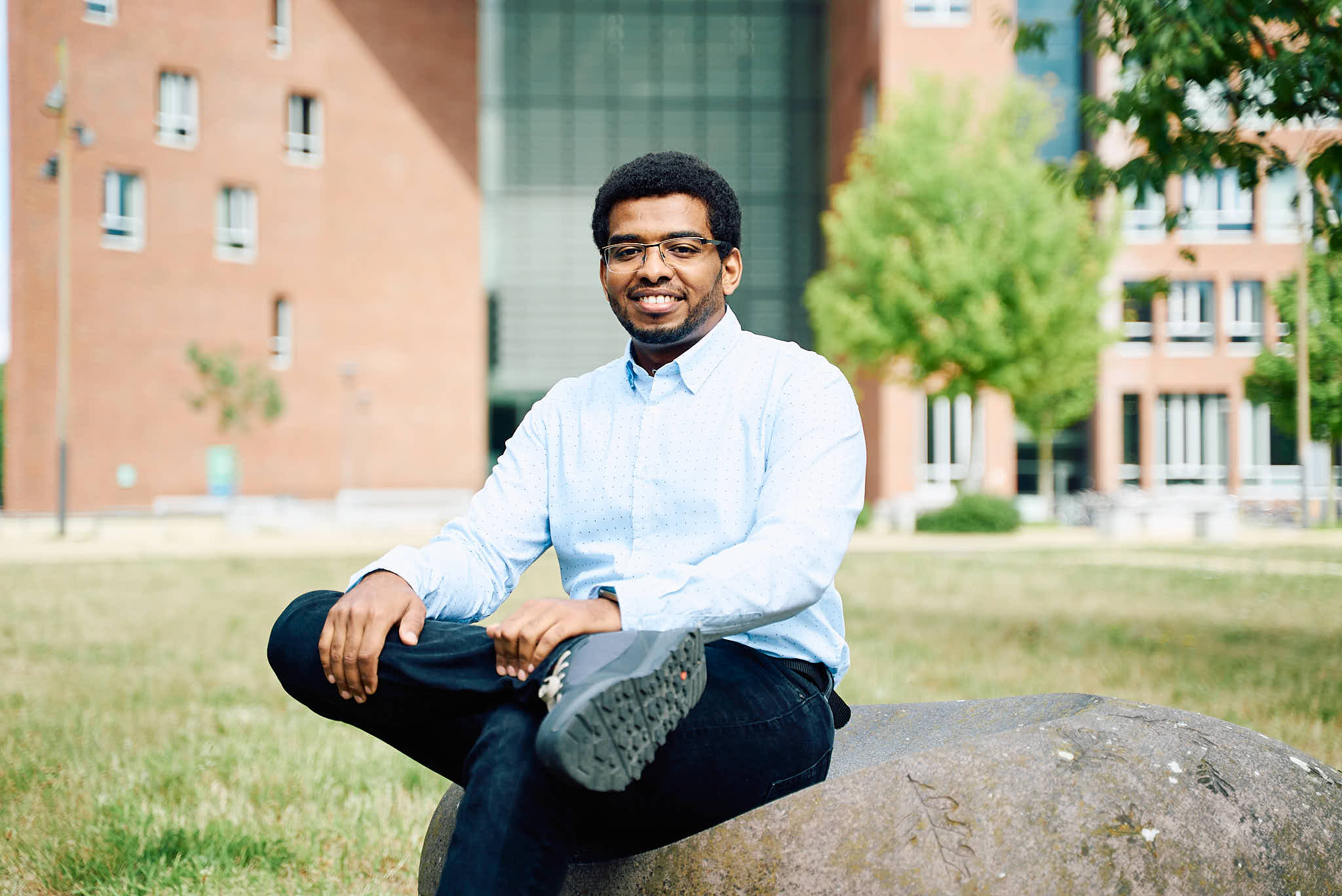 Student Hassan sits on a sitting stone in front of the Forum building