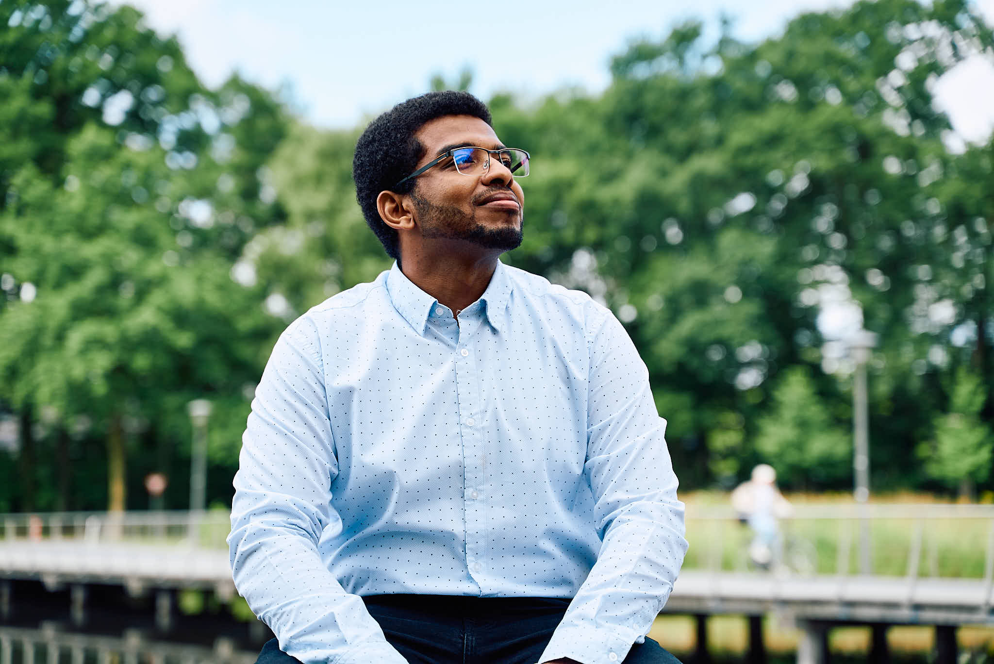 Student Hassan wearing a blue shirt in front of a row of trees