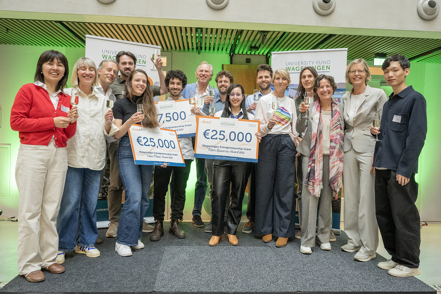 Groep mensen op een podium met drie cheques, twee van 25.000 euro en een van 7.500