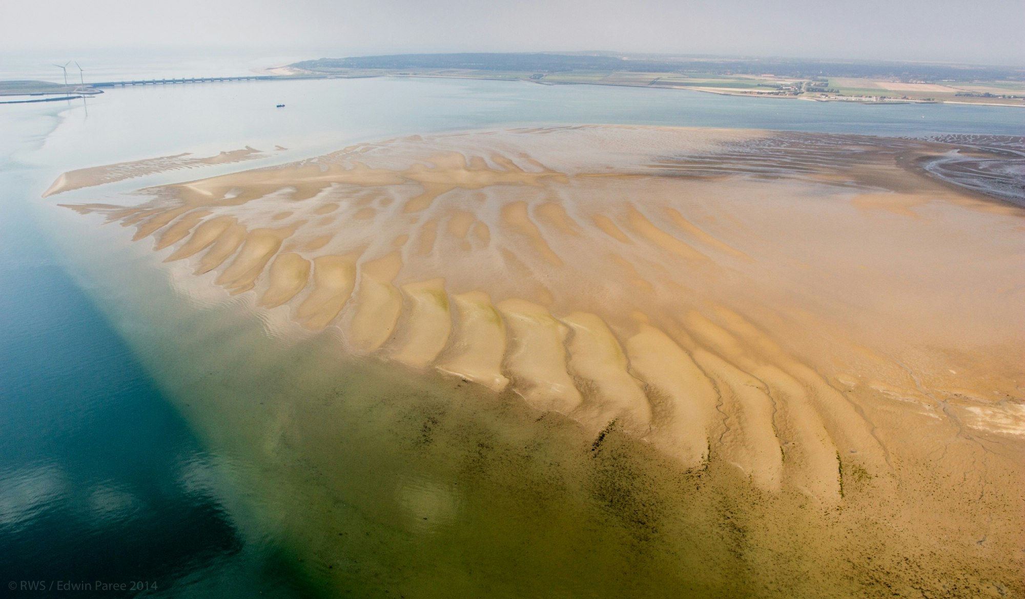 Zandplaat met water en een dam op de achtergrond