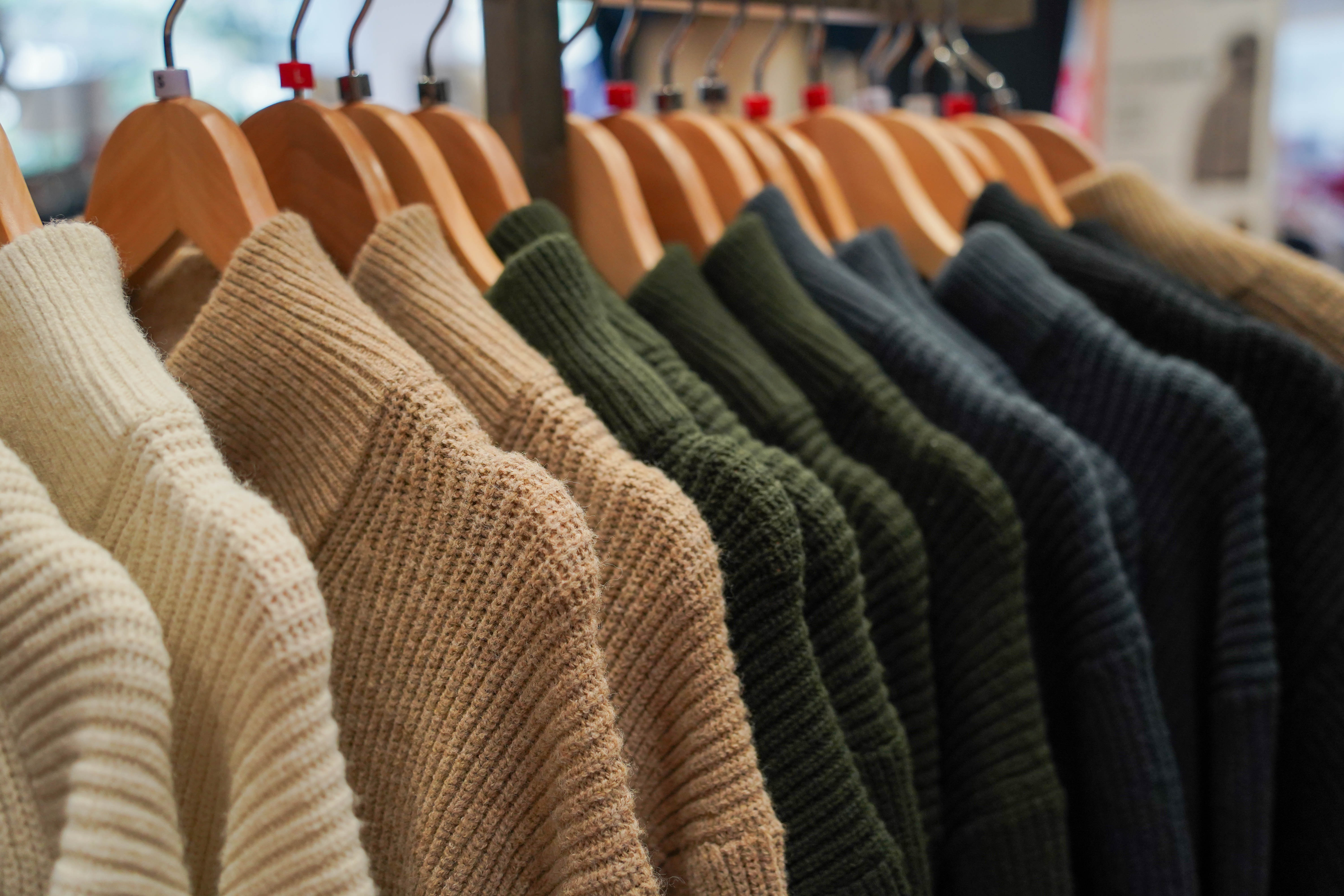 Gekleurde gebreide truien hangen aan houten hangers.