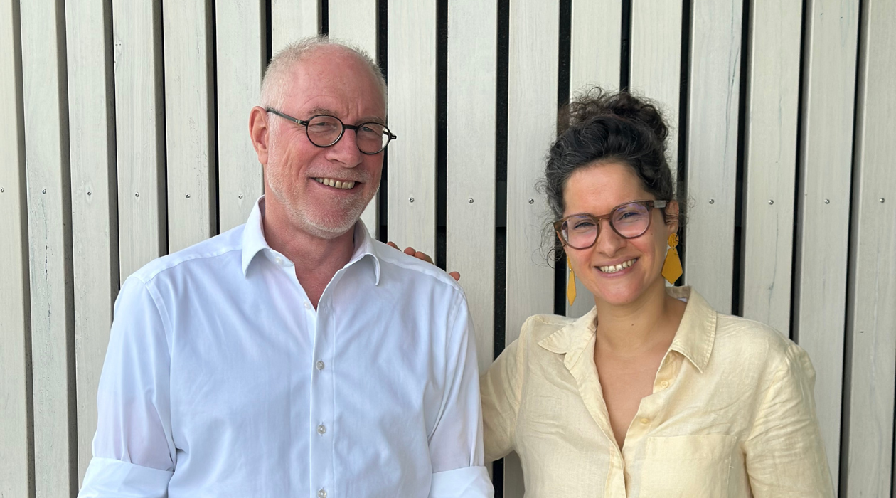 man in white shirt and woman in blue blouse in front of wood panel wall