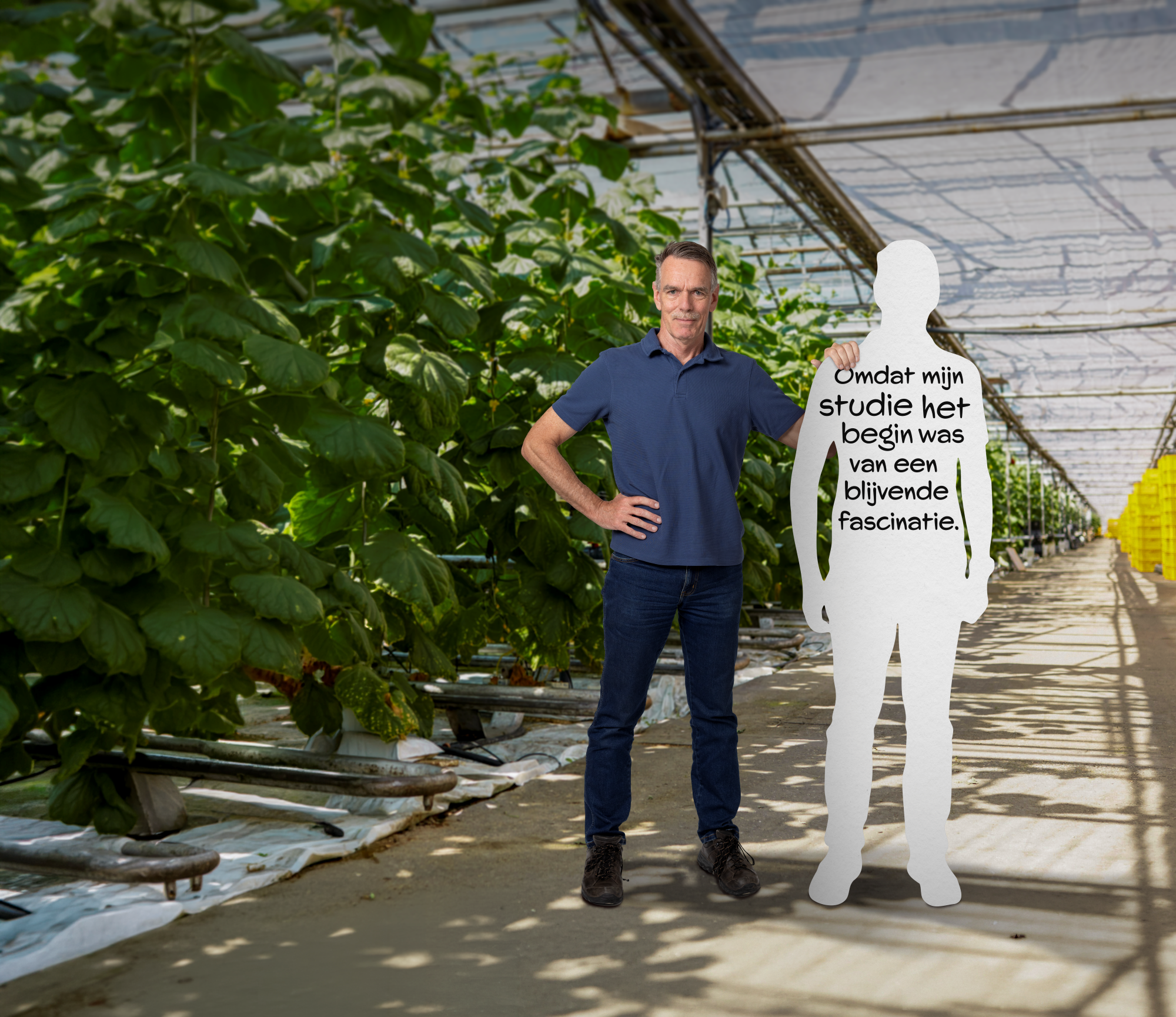 Man in a greenhouse with plants puts a hand on the shoulder of a white cut-out of himself, on which a text in dutch is written.
