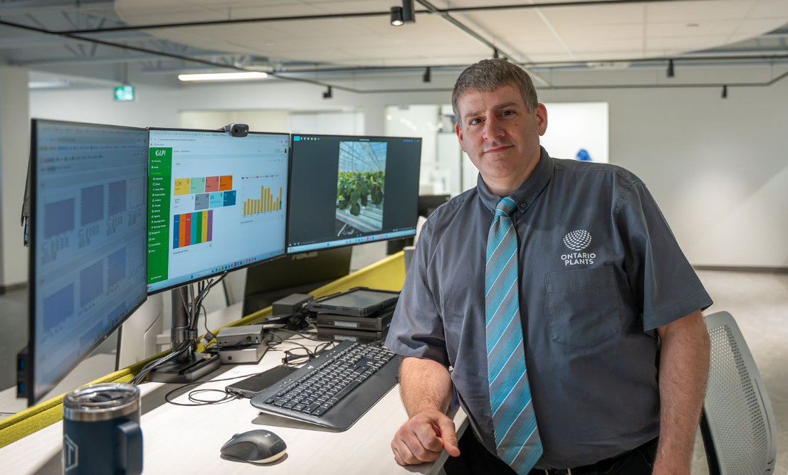 Greenhouse professional beside computer screens displaying crop and greenhouse data