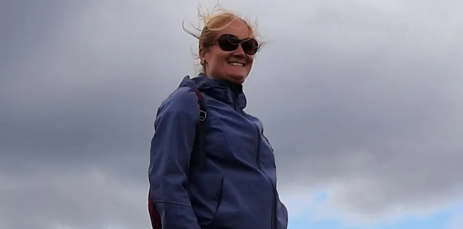 Woman with a blue jacket and sunglasses against a cloudy sky