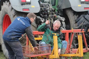 Twee mannen leggen jonge gelabelde boompjes in een krat bij een tractor